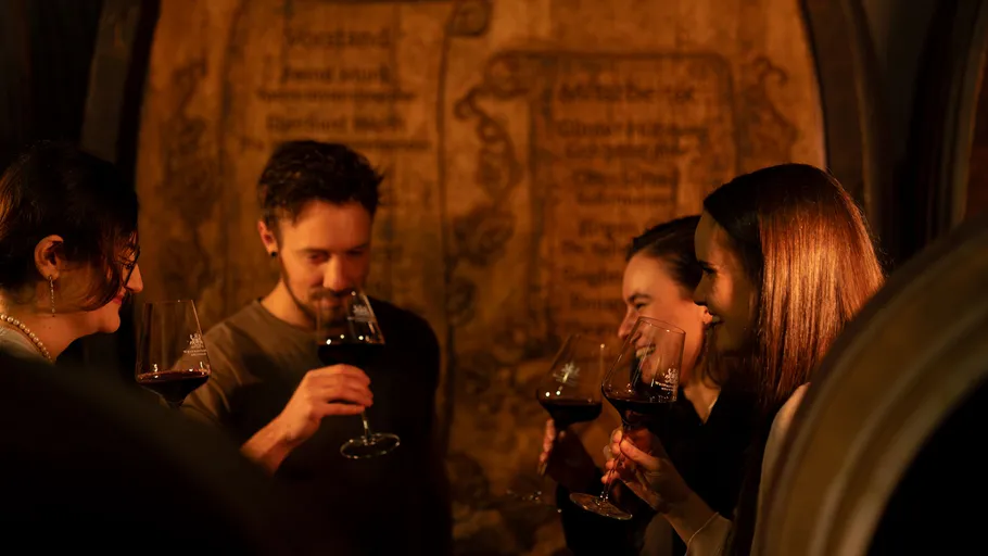 People tasting red wine in a dim cellar.