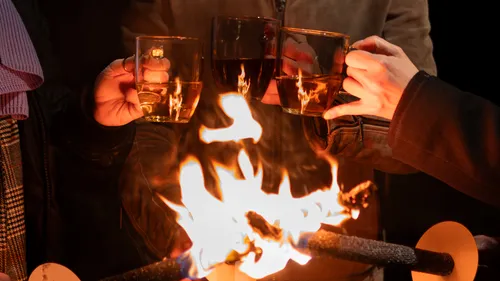 People toasting with cups by a fire.