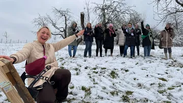 Group of women cheerfully posing in snowy orchard.