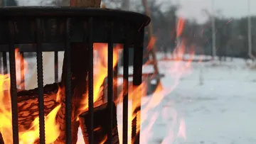 Firewood burning in outdoor metal holder.