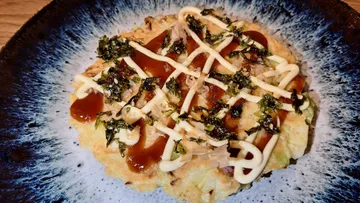 Japanischer Pfannkuchen mit Mayo und Sauce auf Teller.