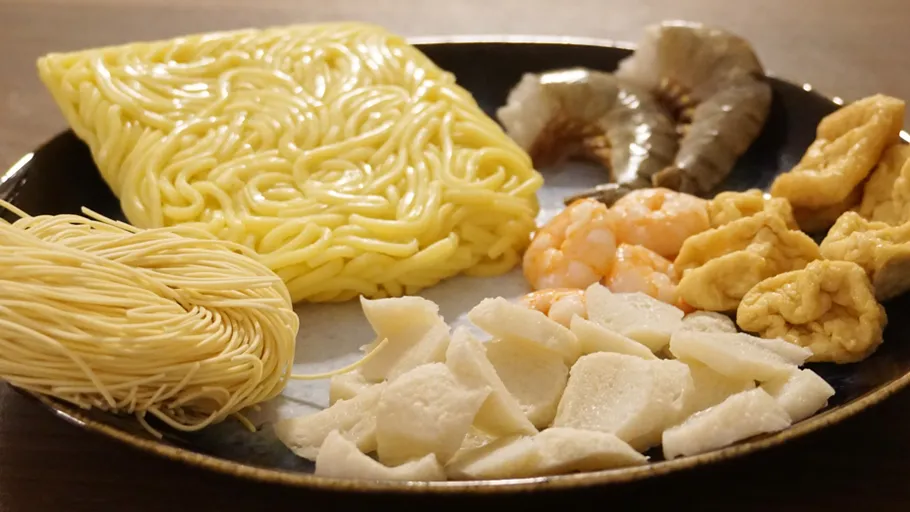 Verschiedene Nudeln, Garnelen, Fischkuchen auf Teller.