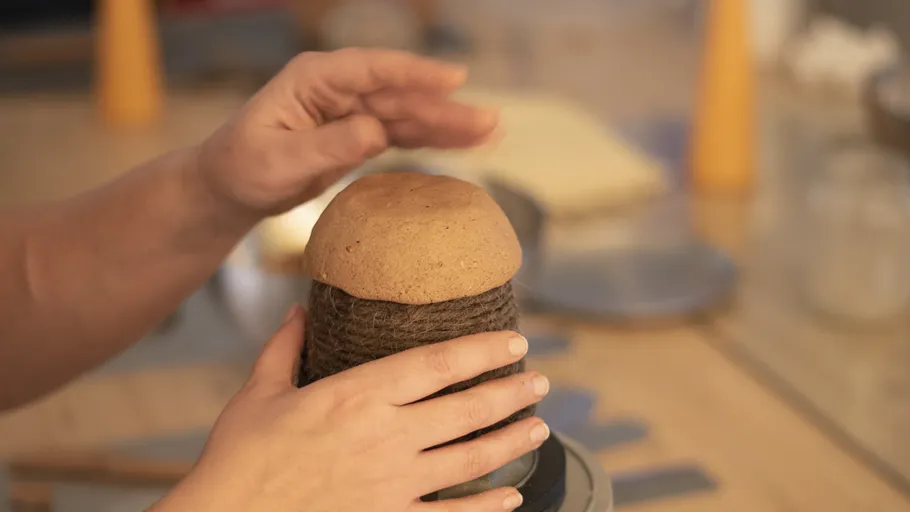 Hände formen Ton auf einer Drehscheibe.