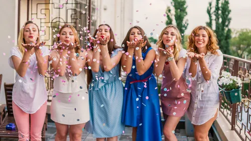 Women blowing confetti on balcony outside.