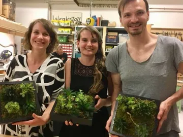 Three people keep plant arrangements in a workshop.