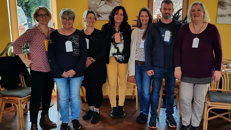 Seven people standing together indoors smiling.
