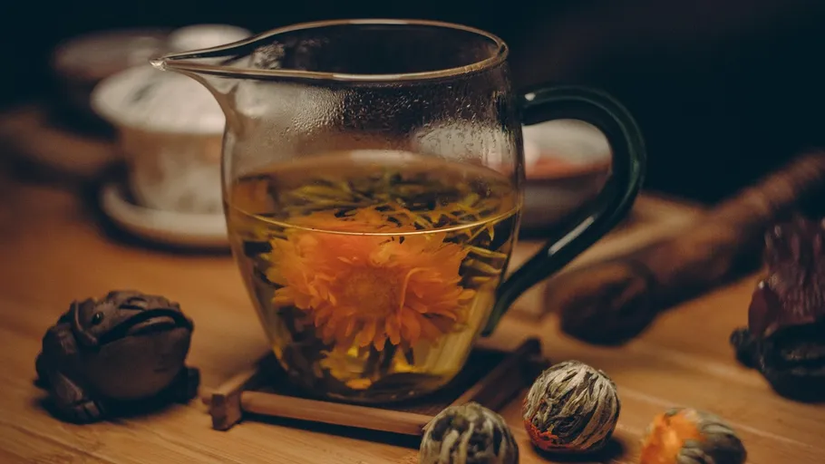 Glass teapot with blooming tea on table.