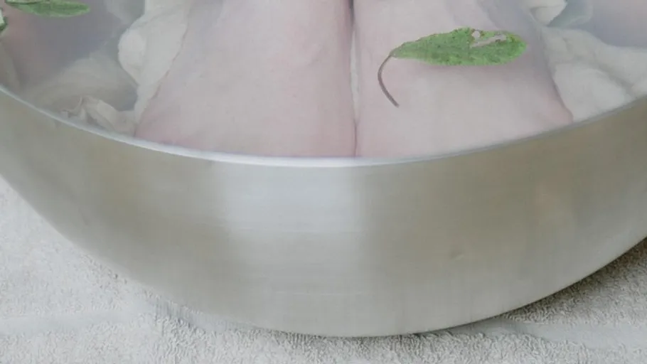 Feet soaking in a metal bowl with leaves.