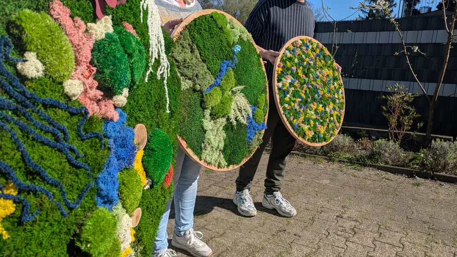 People holding round moss art outside.