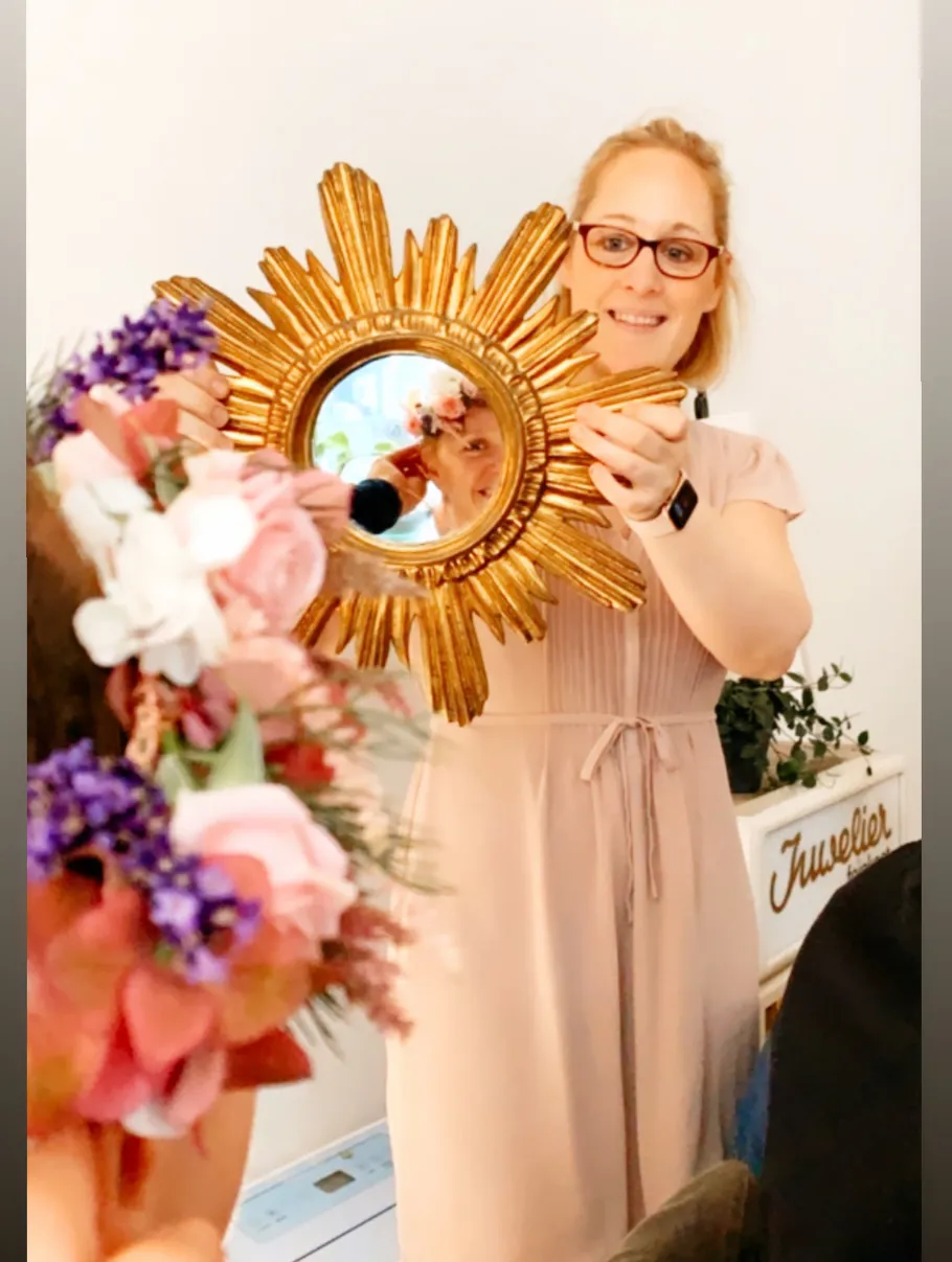 Eine Frau hält einen goldenen Spiegel und lächelt.