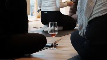 Personen sitzen auf Matten mit Weinglas.