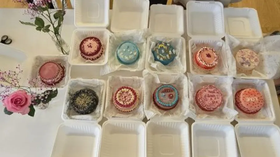 Elf dekorierte Kuchen in offenen weißen Behältern.