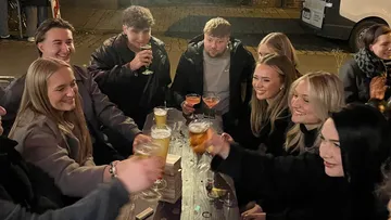 Gruppe stößt Getränke an Tisch im Freien an.