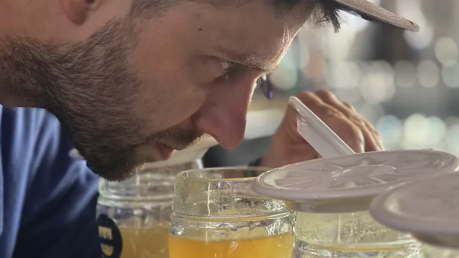 Man inspecting drinks with nose close to lid.