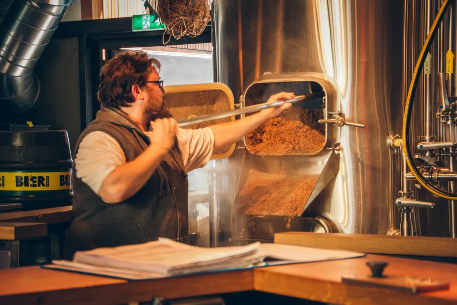 Person cleaning grain mash from brewery tank.