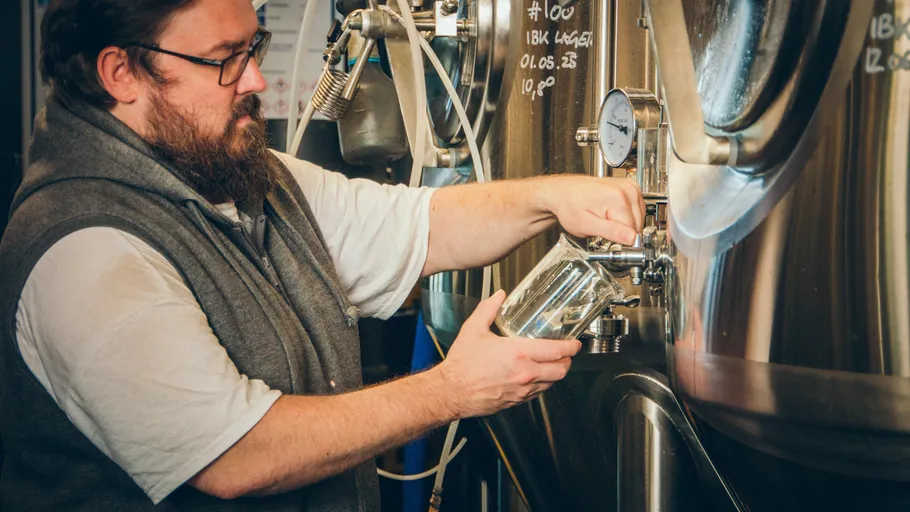 Man pouring liquid from large brewing tank.