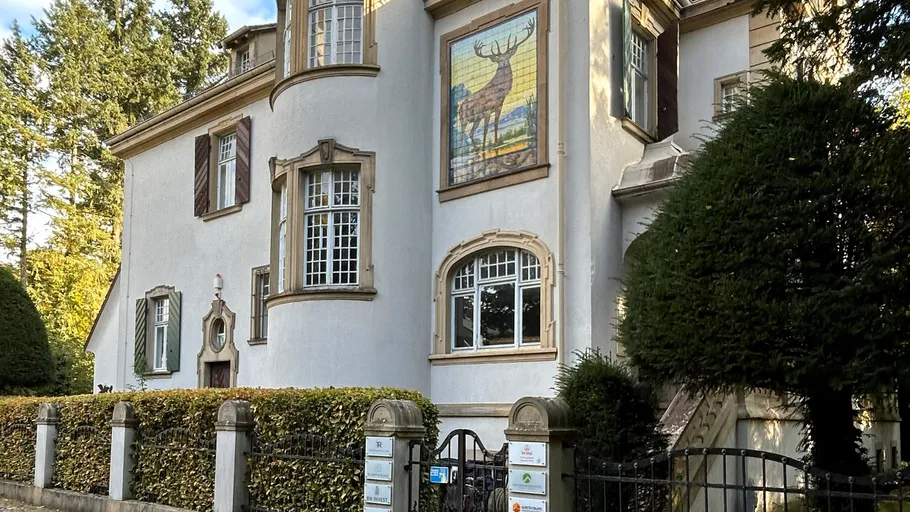 White house with deer mural, surrounded by trees.