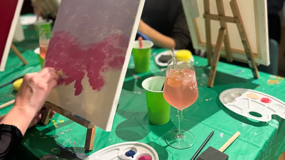 Person painting on canvas, drink nearby.