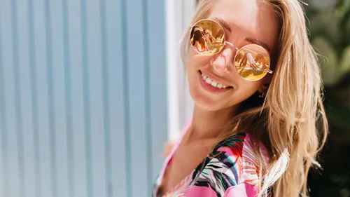 Woman smiling wearing sunglasses, outdoor setting.