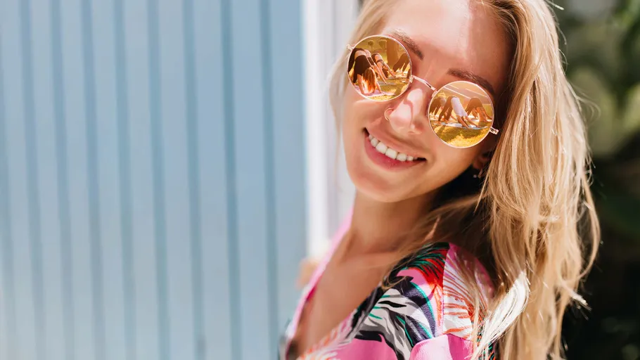 Frau lächelt mit Sonnenbrille, draußen.