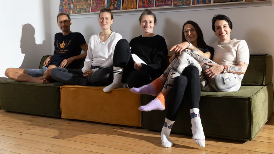 Fünf Personen sitzen auf einem Sofa und lächeln drinnen.