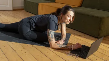 Person dehnt sich am Boden und nutzt Laptop.