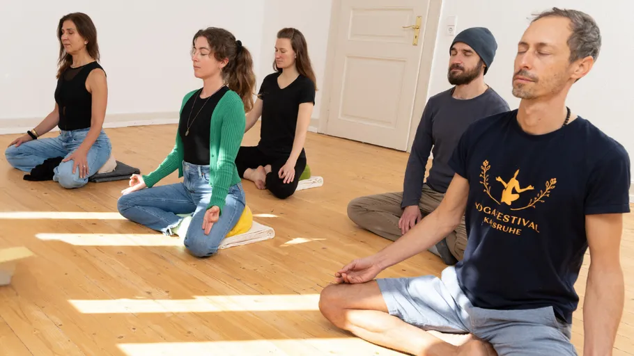 Group meditating on wooden floor indoors.