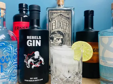 Flaschen und Cocktailglas mit Eis und Limette auf Tisch.