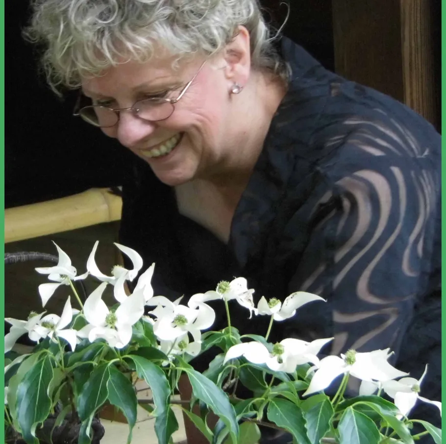 Smiling person tending white flowers indoors.