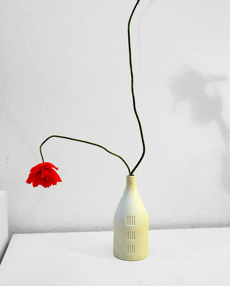 Red flower in a ceramic vase on a table.