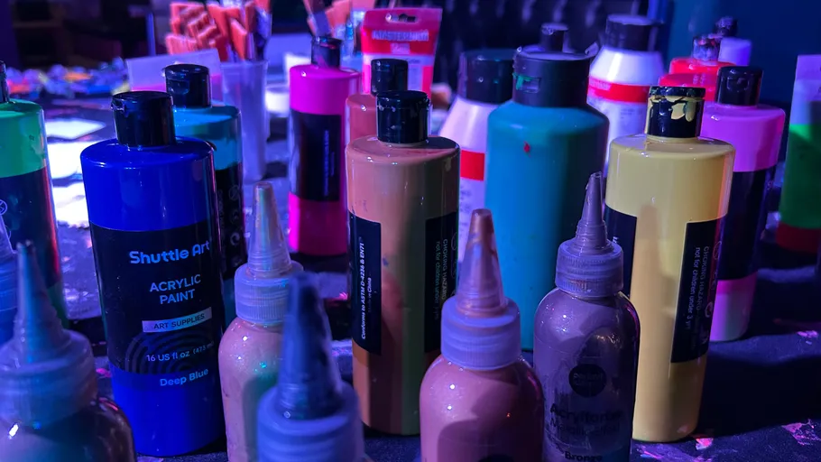 Acrylic paint bottles on a cluttered table.