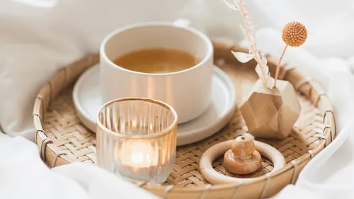 Cup of tea and candle on woven tray.