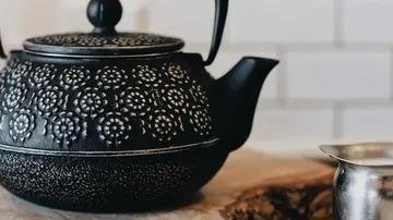 Schwarze Teekanne mit Muster auf Holz.