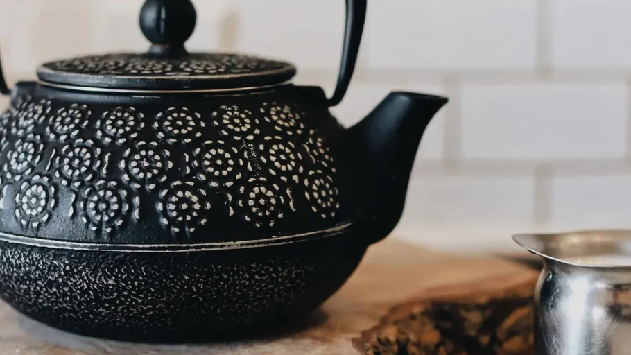 Black teapot with pattern on wooden surface.