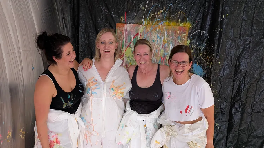 Four women with paint splatters laughing together.