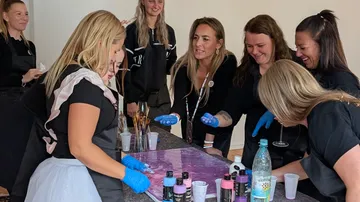 Frauen malen an einem Tisch, lächeln gemeinsam.