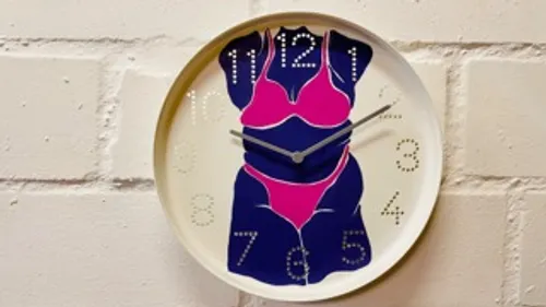 Clock with bikini design on brick wall.