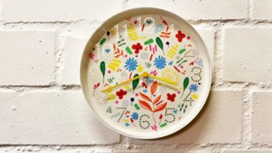 Colorful floral clock on white brick wall.