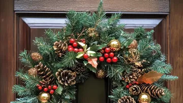 Festive wreath on wooden door, pine cones and berries.