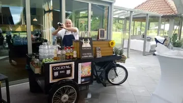 Bartender shaking drink at mobile cart outdoors.