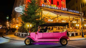 Pink vintage car parked near illuminated cafe.