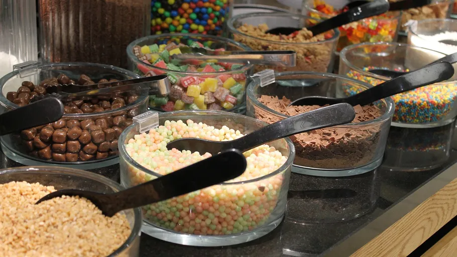 Various candy bowls with scoops on a counter.