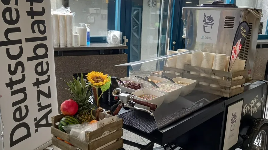 Frozen yogurt cart with toppings and decorations indoors.