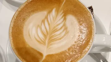 Latte with leaf art in white cup.