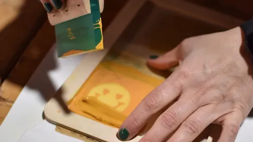 Person screen printing emoji design on fabric.