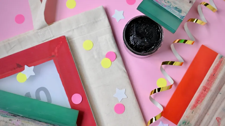 Craft materials and ink pot on pink background.