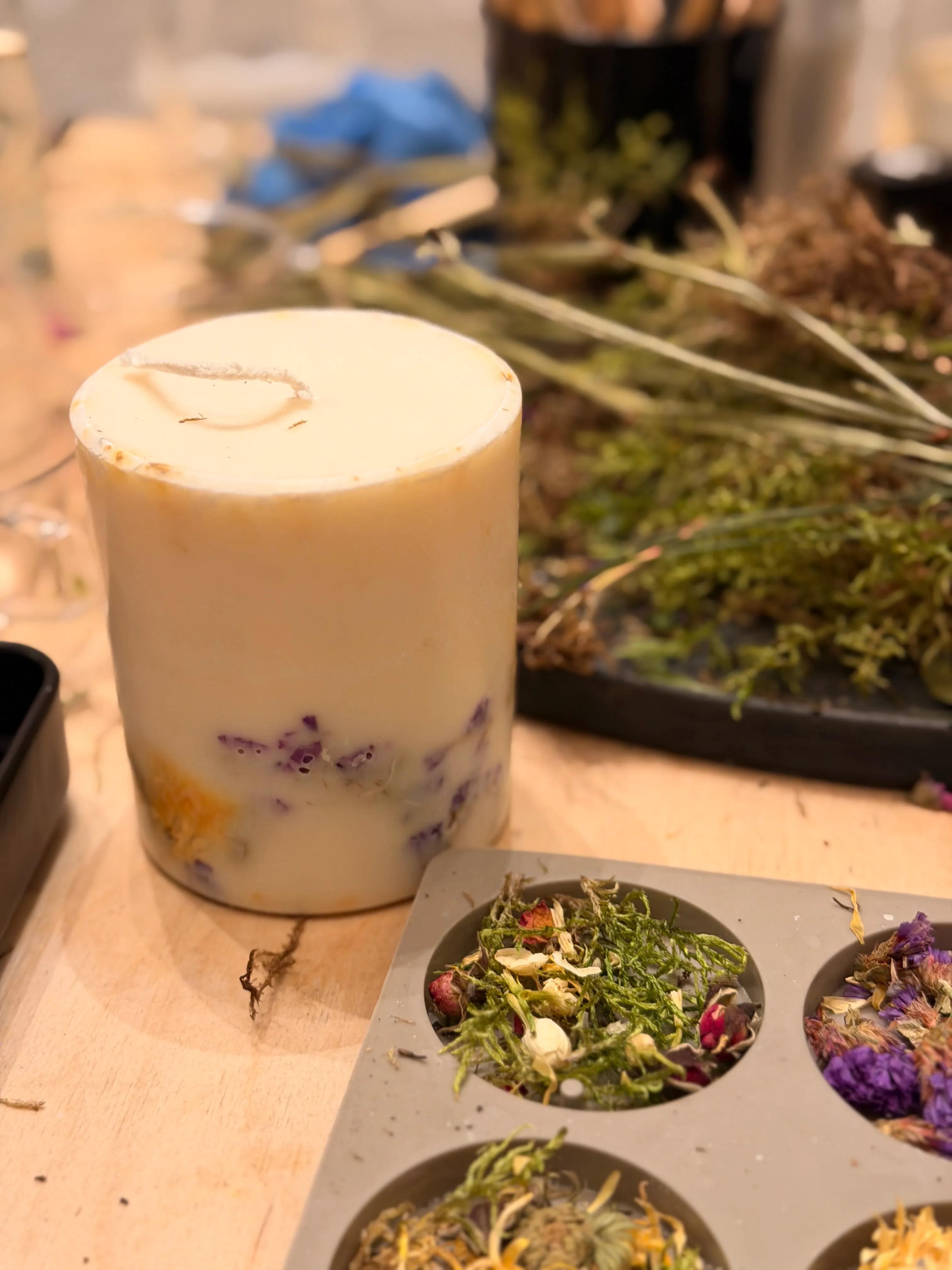 Bunte Kerze mit getrockneten Kräutern daneben.