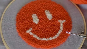 Orange smiley face embroidered on fabric.