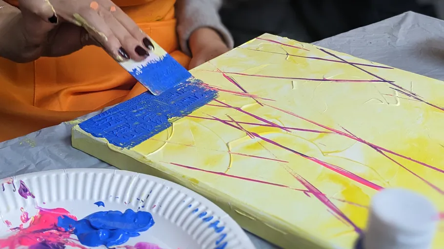 Person painting canvas with blue scraper.