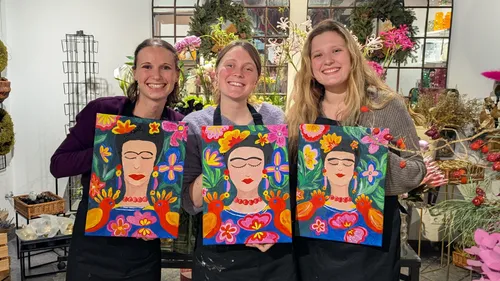 Drei Frauen halten bunte Frida Kahlo Gemälde drinnen.